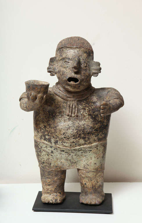 Ixtlan del Rio style.  He stands tall, sensitively yet abstractly molded with ear clips, arm bands, necklace, nose ring, and loin cloth and the he is holding an offering cup in one hand; his lips pursed in the positing of a mourner.