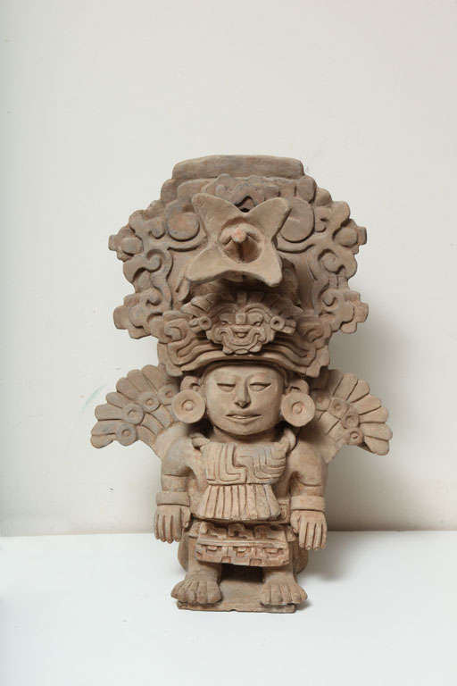 From Monte Alban, Oaxaca. It is a large and museum quality ceramic effigy urn of the  male figure standing with massive rectangular badge suspended from the collar, the symmetrical pleasing face with curved nose and outlined eyes; he is laden with