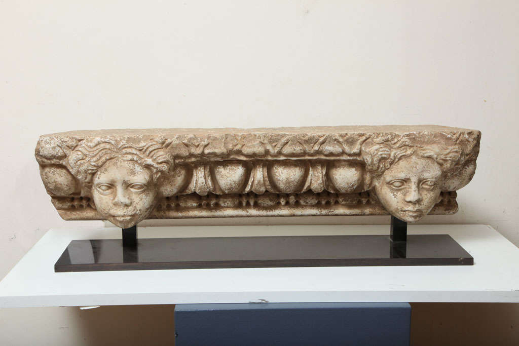 Long and slender architectural entablature carved in relief with two idealized heads with centrally parted wavy hair, the plump faces with large almond-shaped eyes, the heads overlaying and flanking a band of meandering ivy above a deep-cut  row of