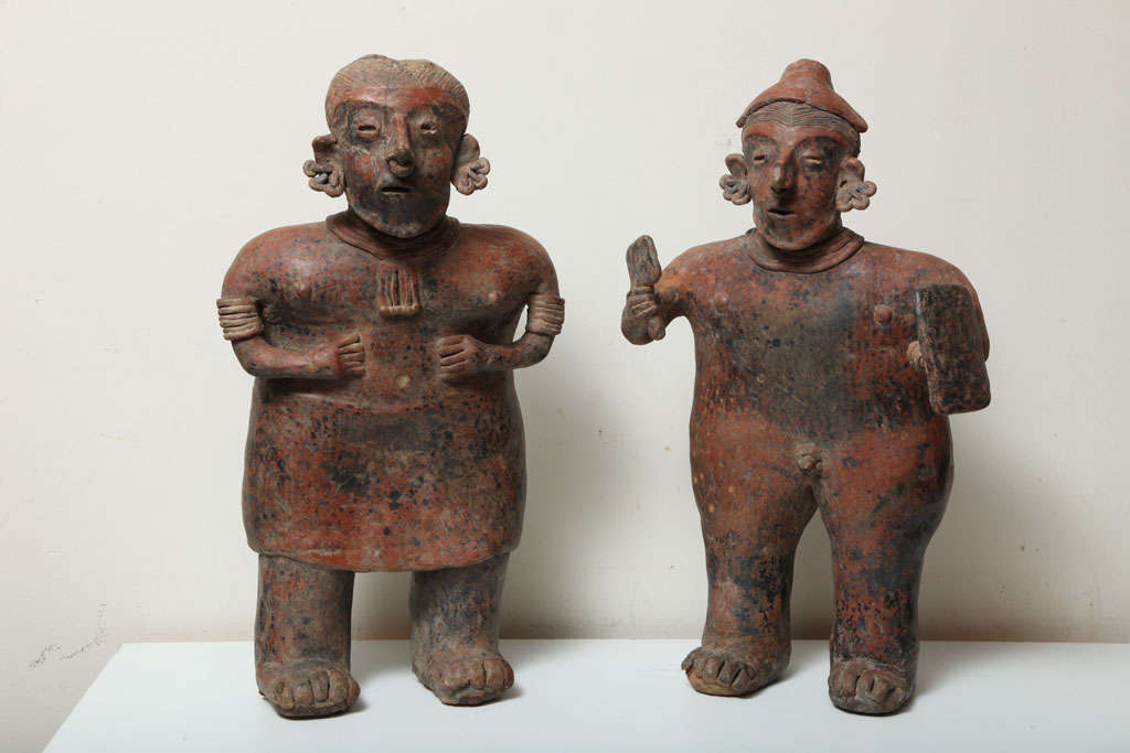 Massive imposing abstracted clay effigy figures of highly stylized forms. He is a warrior with cap-like helmet, mace and shield. She wears a skirt, necklace, arm and ear ornaments. Both, fashioned from the same hand are a true couple, both have red