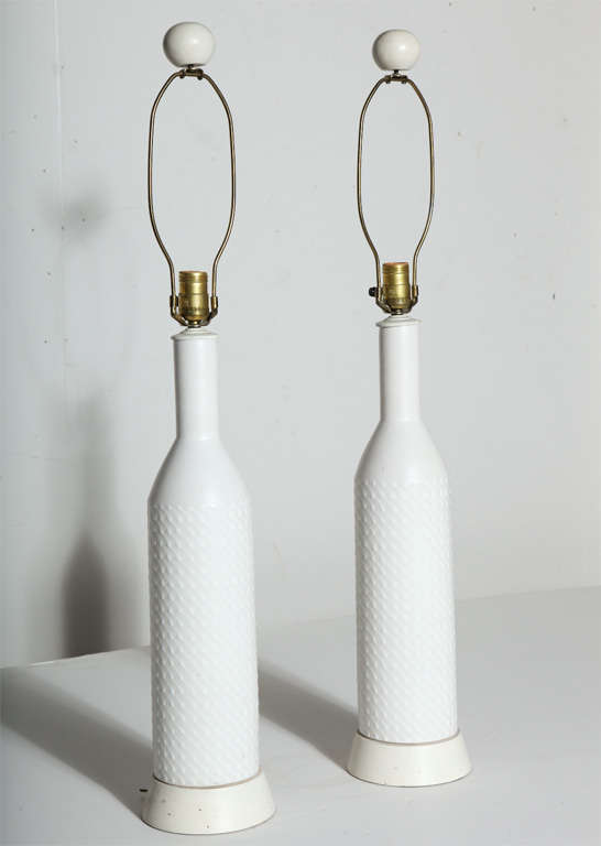 Tall Pair of AK KAG Switzerland  White textured Art Pottery Table Lamps, 1960's. Featuring a  slim bottle form with uniform flowing textured and smooth dot pattern in White glazed ceramic on round  Warm White enameled wood base with original paint,