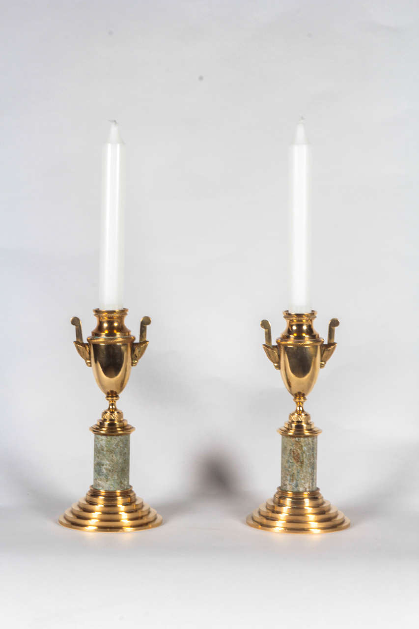 A pair of Swedish Grace brass and Kolmards marble candlesticks, Circa 1930, each with an urn form candle holder above a circular column support raised on a circular stepped base. The urn candle holder can be turned over when not in use to create a