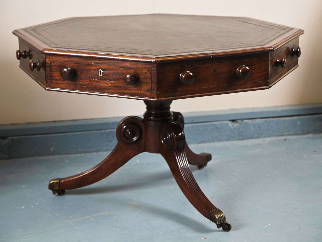 In a departure from the circular norm, this octagonal table has a rotating top with four functioning drawers and four dummy drawers, each with wood pulls. The three splay legs to the pedestal have carved decoration and terminate in brass toe caps