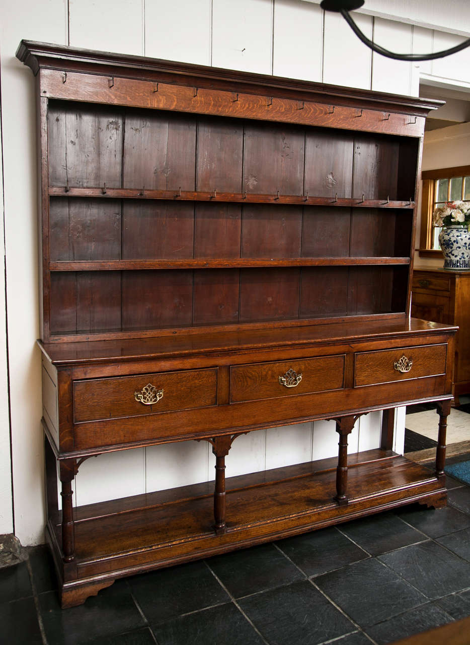 This Georgian oak potboard dresser with three drawers and supported by turned stiles has a unique graduated rack with the deepest shelf at the top and the shallowest at the bottom, allowing for display of larger items up closer to the line of sight.