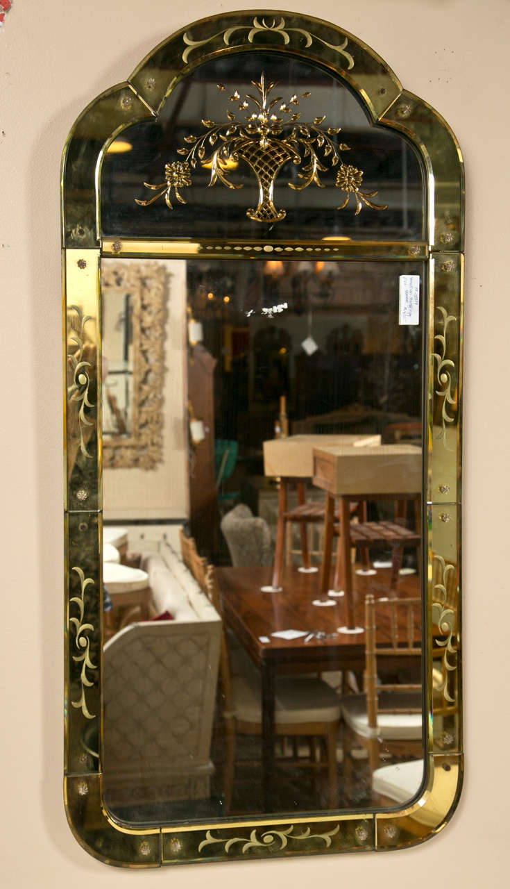 A Venetian Etched Glass Eglomise Wall Mirror. This delicate wall mirror having a center clear mirror panel framed in a gilt gold leaf and vine design border terminating in a gilt flower basket with floral arrangement. Rectangular in shape.