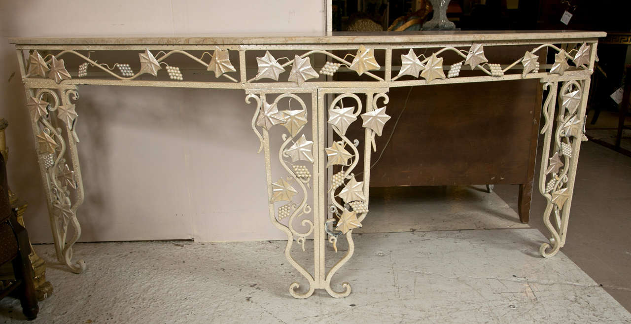 Intriguing Art Deco style console table. The beige irregular shaped marble top supported on a painted iron base depicting vines and grape style. Can be used inside or outside.