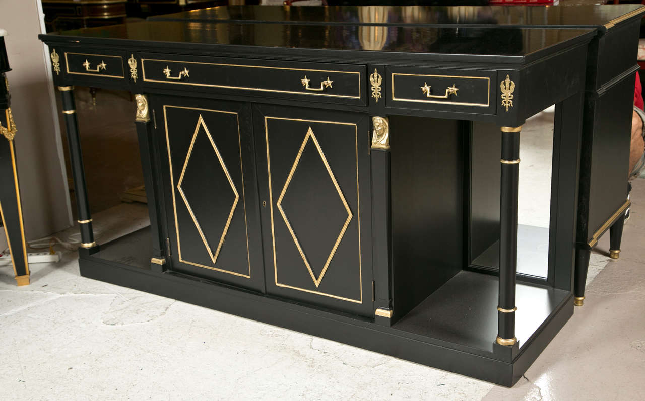 An Empire style sideboard, circa 1940s, overall ebonized and decorated with bronze mounts, the rectangular top over a narrow frieze fitted with three banded drawers, atop a central two-door cabinet with diamond-shape banded front, and a circular