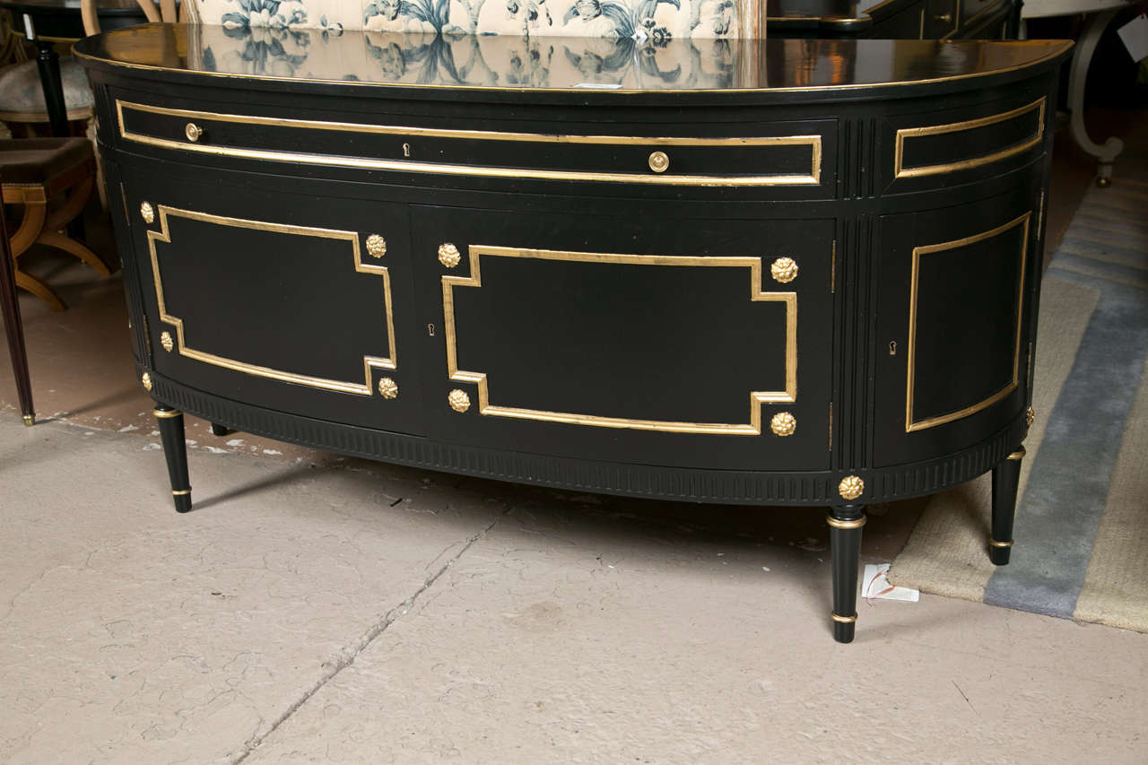 A grand French Directoire style sideboard, overall ebonized and parcel-gilt, circa 1940s, the large bow-shaped top over a narrow banded frieze, atop an enclosing double-door cabinet, each side also has a single-door storage unit, raised on tapering