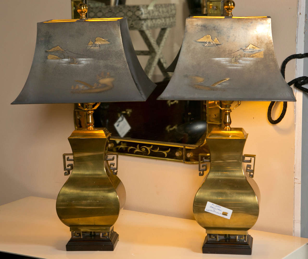 Pair of intriguing brass table lamps in Hollywood Regency style, of urn form and decorated with Chinoiserie style handles, raised on footed and wooden base, come with tole shades.