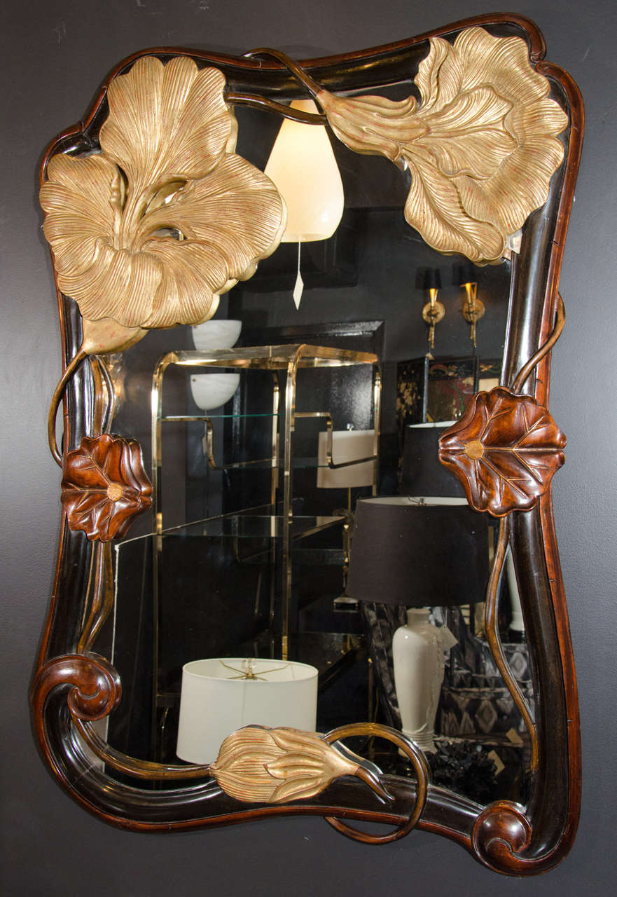 Striking Art Nouveau mirror with outstanding hand carved designs. The mirror features a mahogany frame with exquisite and highly stylized carved details of stems and lotuses or lily florals with parcel gilt finishes. Beautifully exemplifies the very