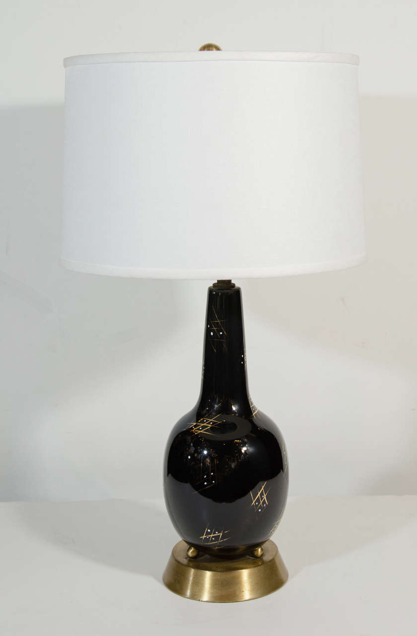 Pair of modern table lamps with elegant sleek forms in black glazed ceramic with hand applied gold leaf geometric patterns. The lamps have dark brass bases and feature stylized brass ball feet. Newly rewired and shown with custom linen drum shades