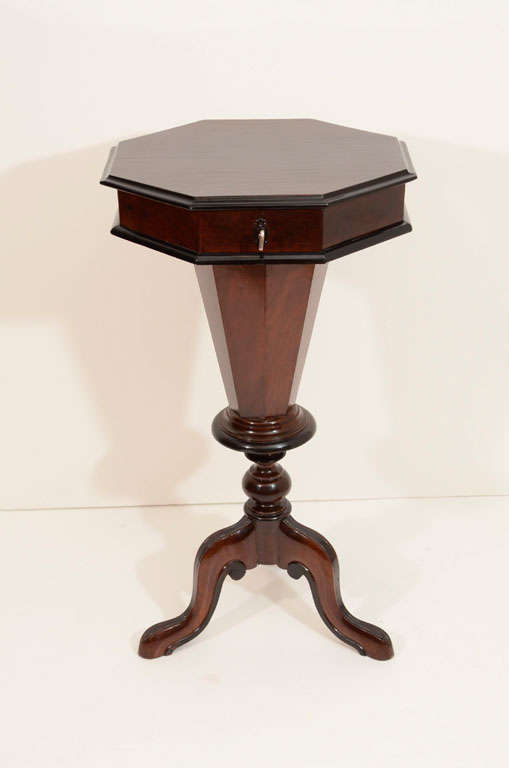 An octagonal pedestal table with a locking, hinged, lid which rises to reveal eight compartments for spools, threads or collectables and a deeper centre compartment for knitting materials.