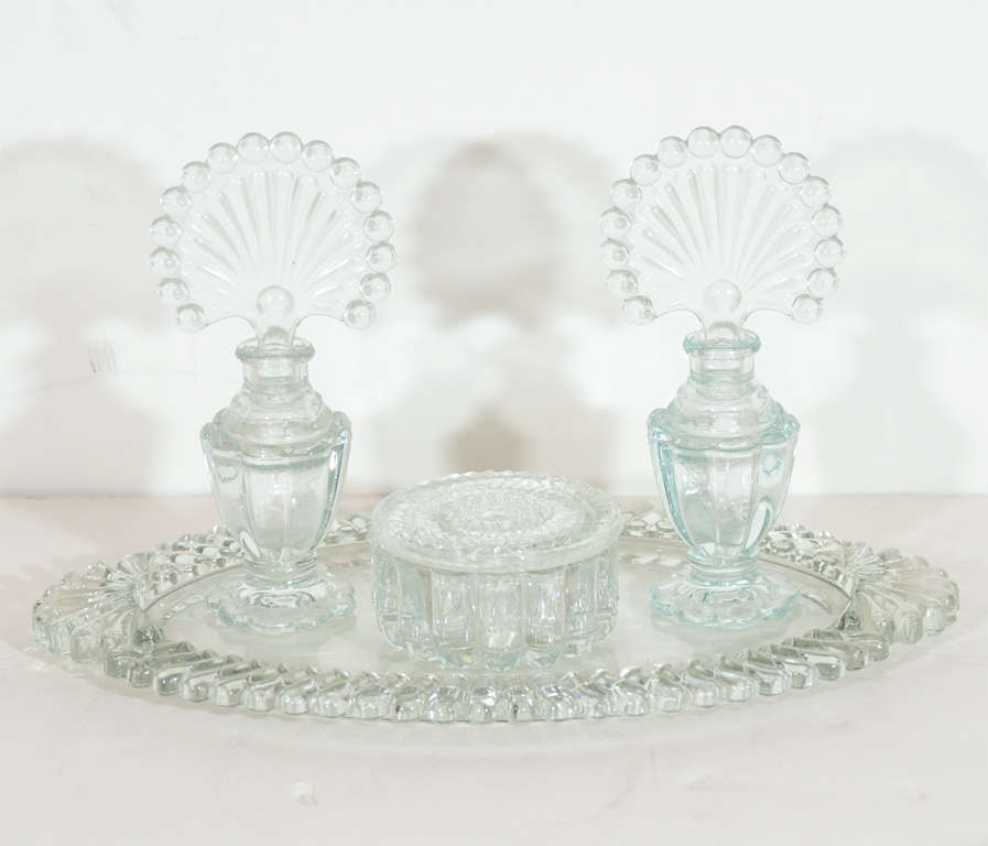 This beautiful set comprises an oval tray,two perfume bottles and a puff box   All with a Art Deco peacock style motif in pressed glass.