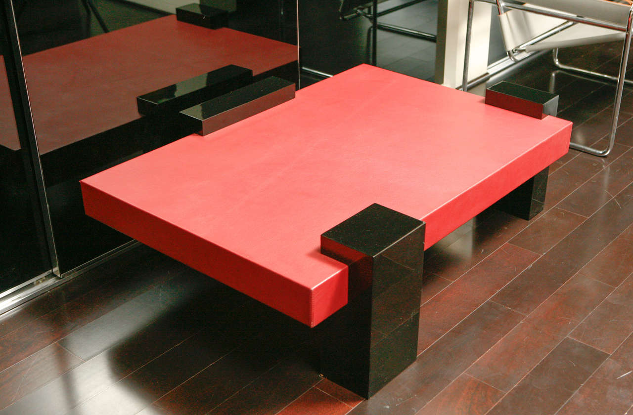 Modernistic coffee table in red leather with three black lacquer feet.