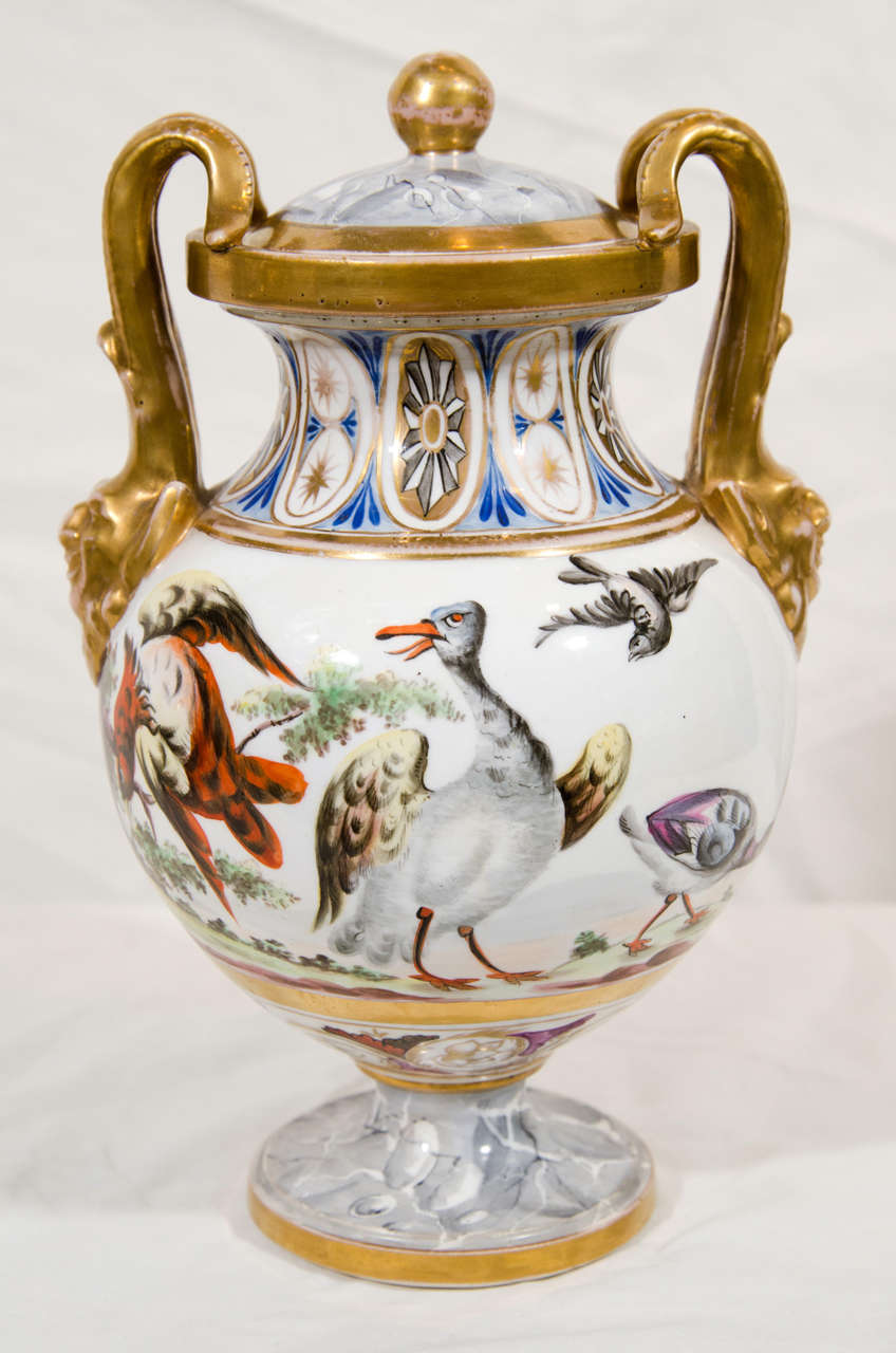 A small covered urn with a lively scene of fanciful birds.The design combines neoclassical and rococo elements including:
a row of medallions, a gilded finial above a faux marble top, and satyr head mask handles.