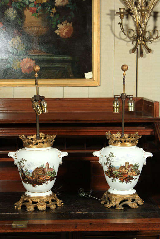 A BEAUTIFUL PAIR OF  CONTINENTAL PORCELAIN VASES, NOW MOUNTED AS LAMPS WITH GILT BRONZE TOP AND BASE. HANDPAINTED SCENIC VIEWS OF CASTLES, GILT HIGHLIGHTS  TO HANDLES