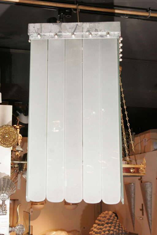 Glass deco ceiling light with loose hanging panels which shade the bulbs. Glass hangs from a square metal frame, bulb is suspended in the middle. Small metal pearl-like balls adorn the top rim.
