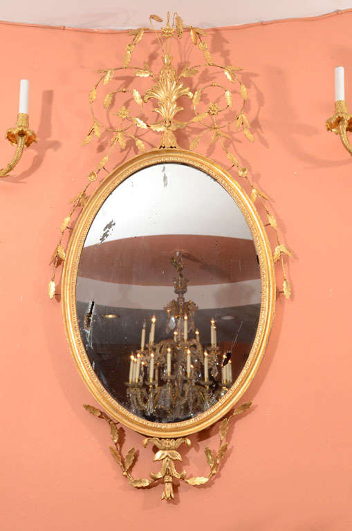 A fine pair of Hepplewhite giltwood oval mirrors with carved pineapples, sheaf of wheat, leaves and acanthus.