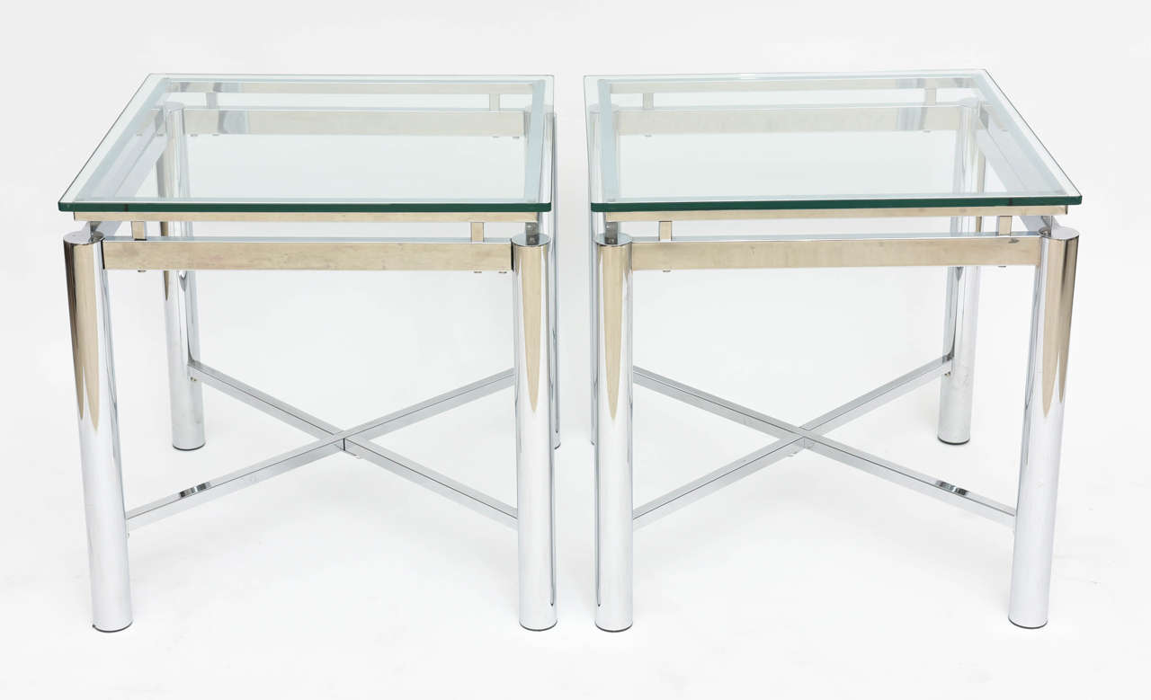 The glass tops above a framework of flat chrome and rounded chrome. The legs columnar and joined by a cross stretcher. Paper label to underside of one table. Two pairs available.