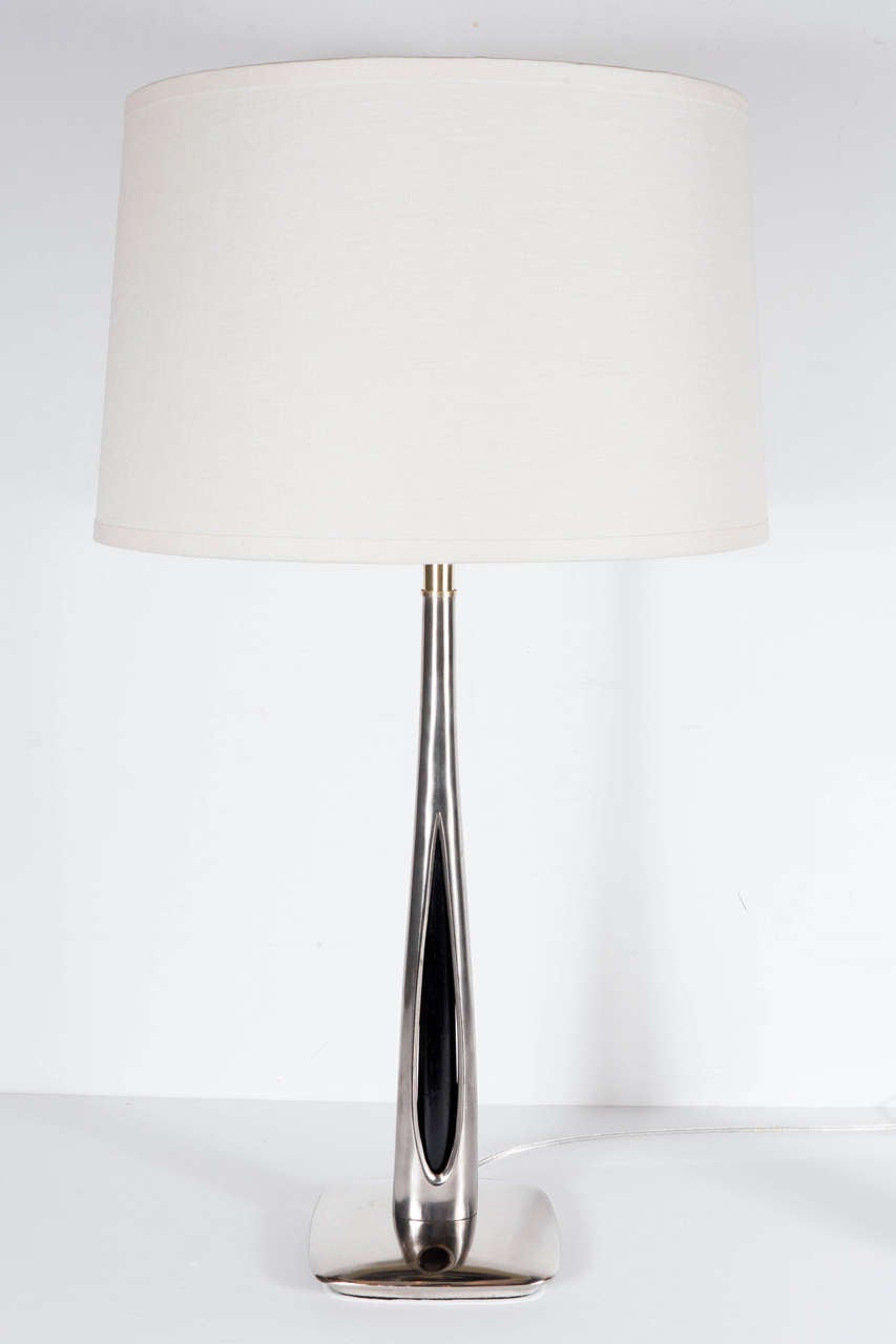 This sophisticated pair of Mid-Century Modernist table lamps feature a brushed nickel streamlined design with a teardrop cut-out that runs along the stem to reveal an ebonized walnut insert. The neck and fittings of the lamps are brushed brass. They