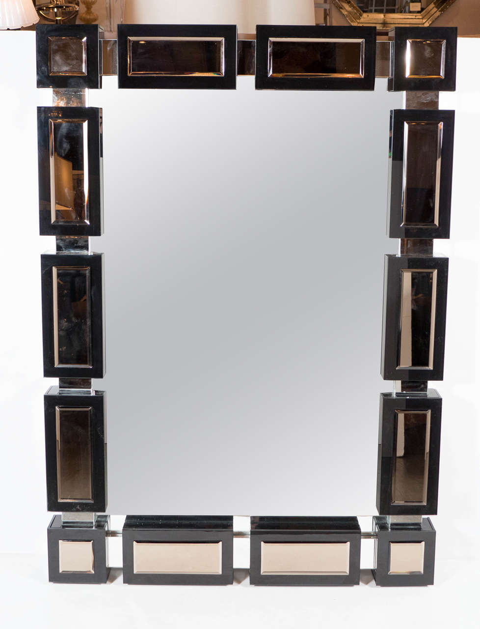 This Mid-Century Modernist mirror consists of a bold segmented geometric design of black mirror on clear mirror. The border features three dimensional rectangular and square segments separated by narrower mirror sections. Each segment has a hand