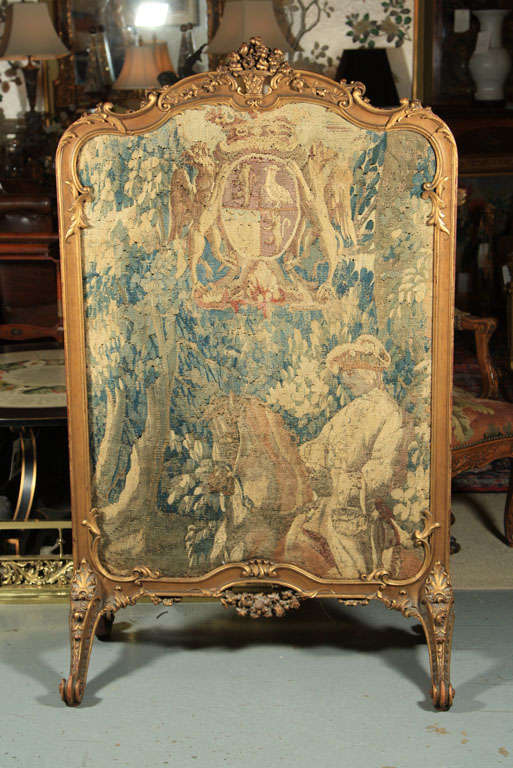 An antique carved and gilt Rococo style fire screen with a tapestry of a horseman in a forest surmounted by a coat of arms.  The tapestry is 18th century and the frame is late 19th century.