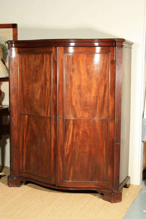An 18th century English Mahogany serpentine front two door clothes press having four shelves and two interior drawers.