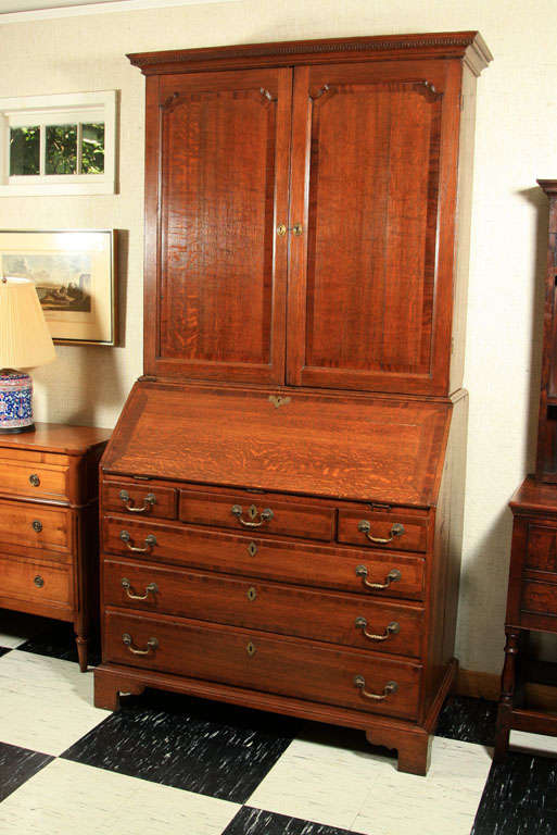 This English oak slant front bureau bookcase / secretary with mahogany crossbanding and dentil crown moulding is a fine example of English country formal furniture. From its shaped, recessed panel doors to its fully outfitted interior of drawers and