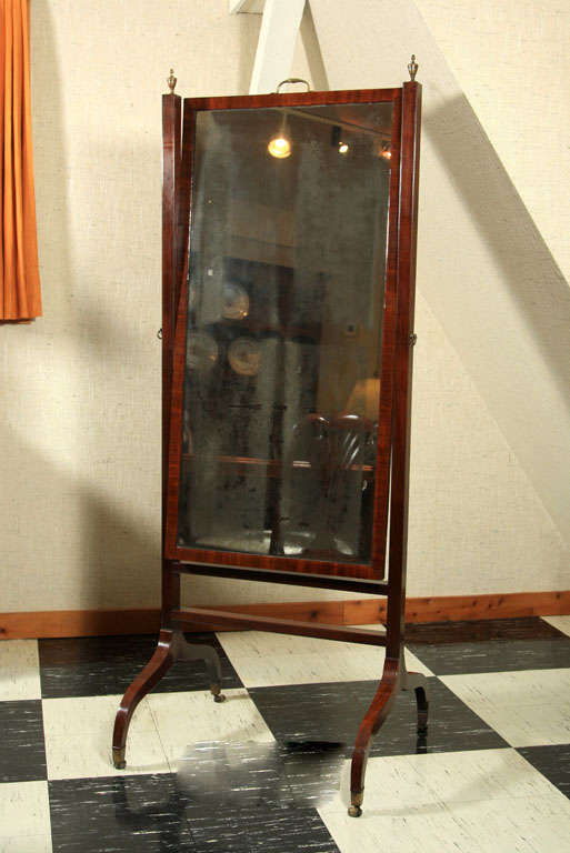 English Regency mahogany cheval mirror with brass urn finials, handle and casters. Maintains original glass.