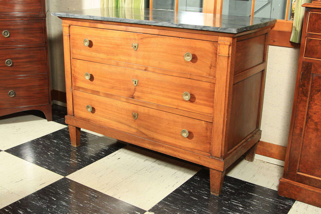 French Empire walnut, marble-top three-drawer commode with brass pulls and shield escutcheons. The columns flanking the drawers and the recessed panel sides lend a refined tone to the clean, bold grain of the walnut wood.