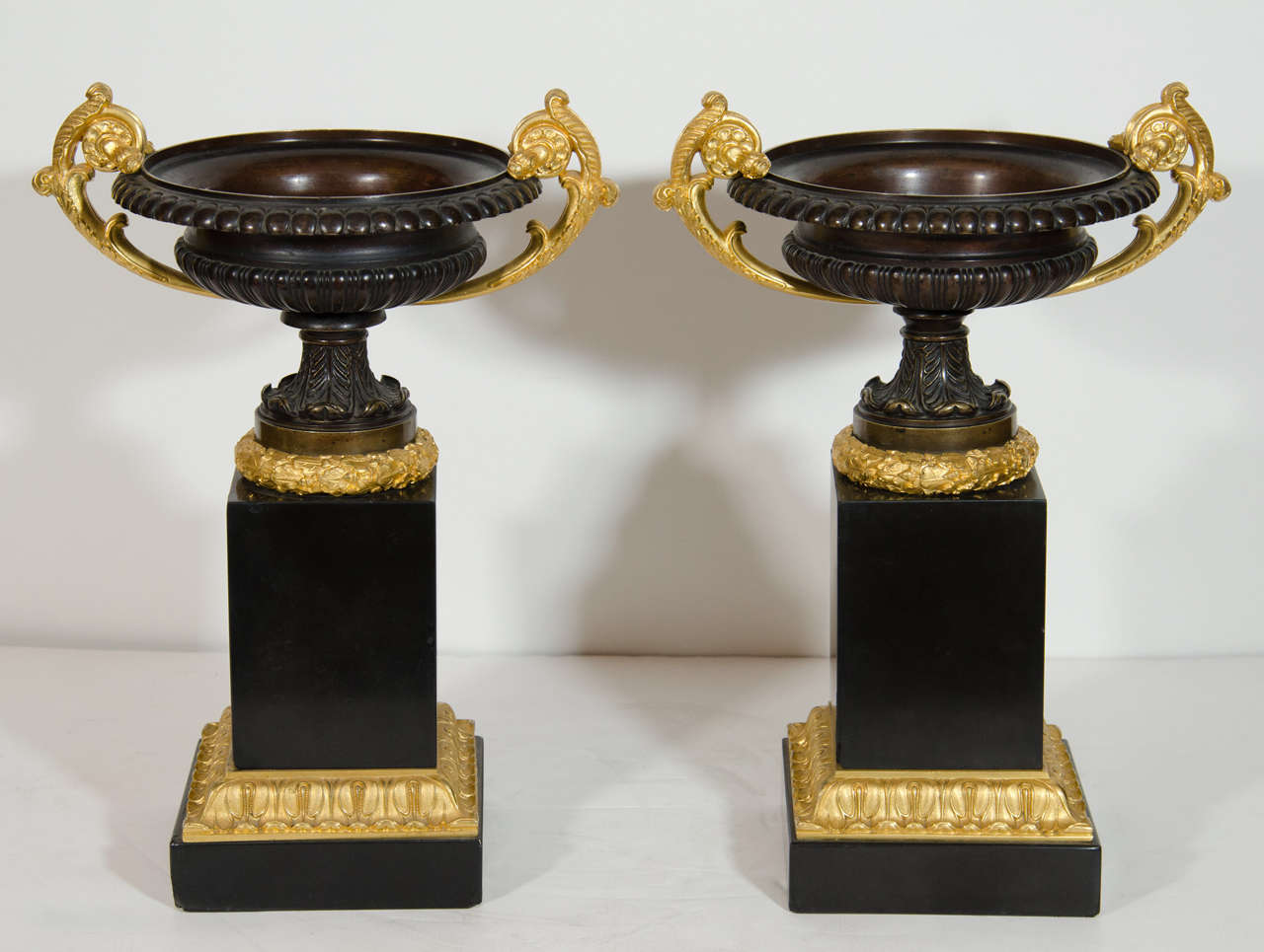 Pair of fine antique French gilt bronze, patina bronze, black marble neoclassical champagne form urns of superb quality embellished on square hand carved black marble bases and further adorned with neoclassical gilt bronze handles.