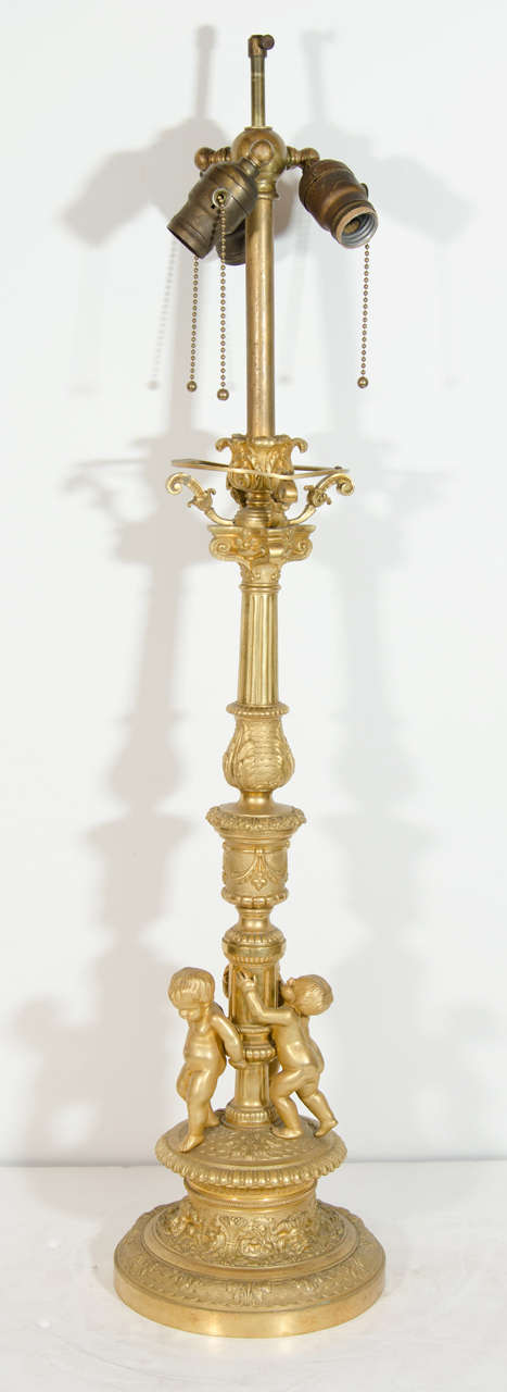 Lampe figurative ancienne de style Louis XVI en bronze doré de très belle facture, reposant sur une base circulaire en bronze doré à motifs fins et ornée de trois figures de puttis.