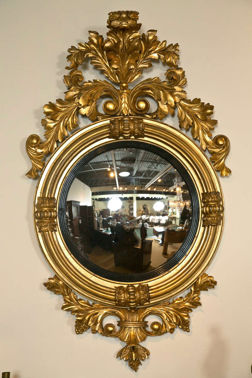 A well carved and gilded early 19th century English or American Regency Period convex mirror with fluted ebonized border to the looking glass surmounted by stylized leaf carvings in excellent condition, circa 1830.