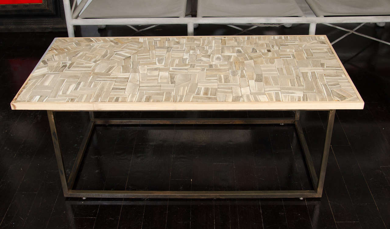 A mosaic coffee table with bone inlay set in a wood frame. The base is a rectangle of steel.