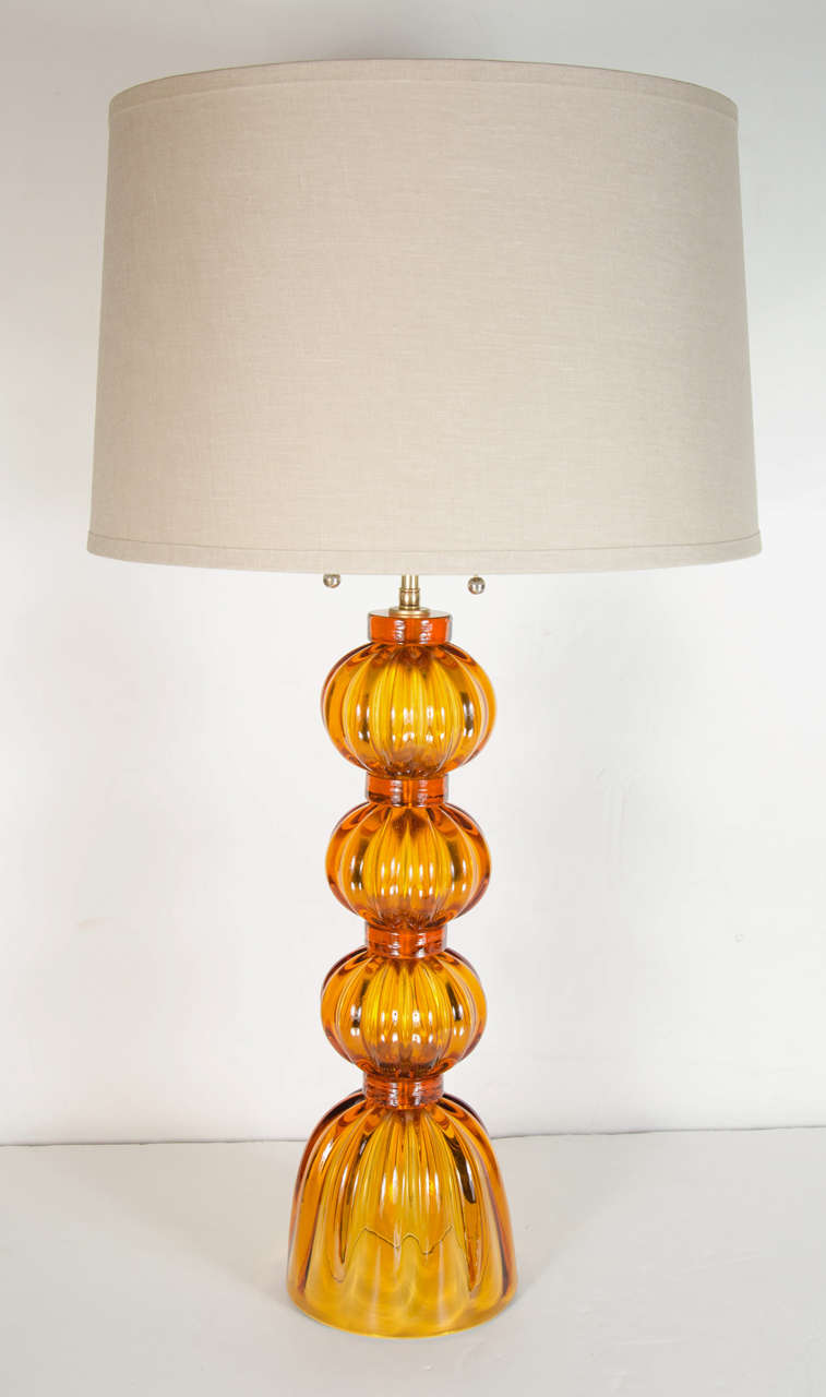 Pair of Mid-Century Modernist hand blown Murano glass table lamps.  These stunning lamps are featured in a rich, vibrant Amber glass that has a ribbed, fluted detailing.  These lamps are comprised of three spherical shaped sections with a dome like
