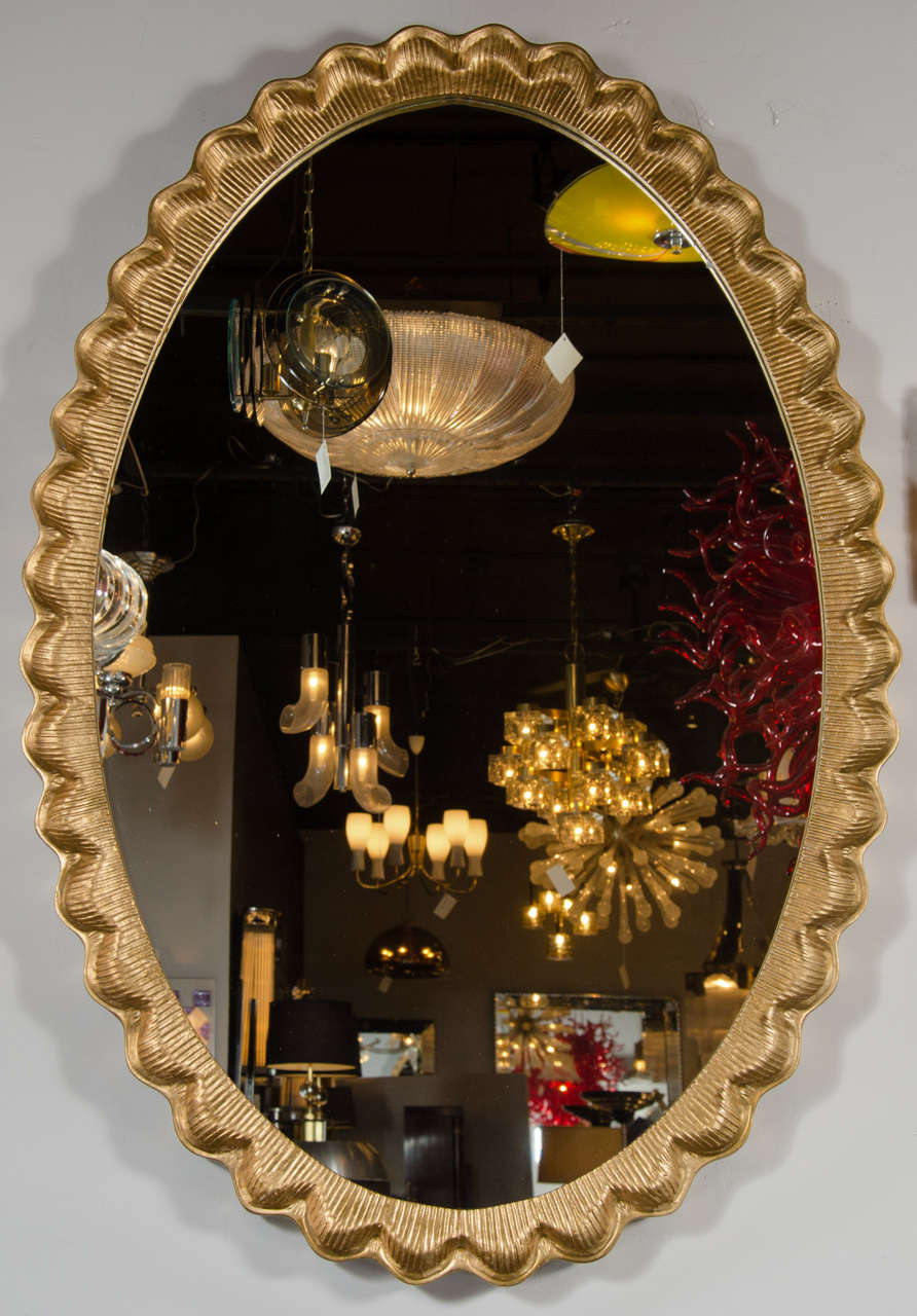 This mirror features a scallop design in 24k Gilt in a modernist ovoid shape by the renown Dorothy Draper. It can be hung vertically or horizontally.
