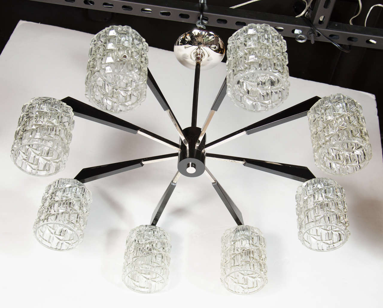 This graphic  Mid-Century Modern chandelier was realized in Denmark, circa 1960. It offers eight arms emanating from a cylindrical body in ebonized walnut with a chrome finial of the same shape adorning its base. The chrome arms have geometric