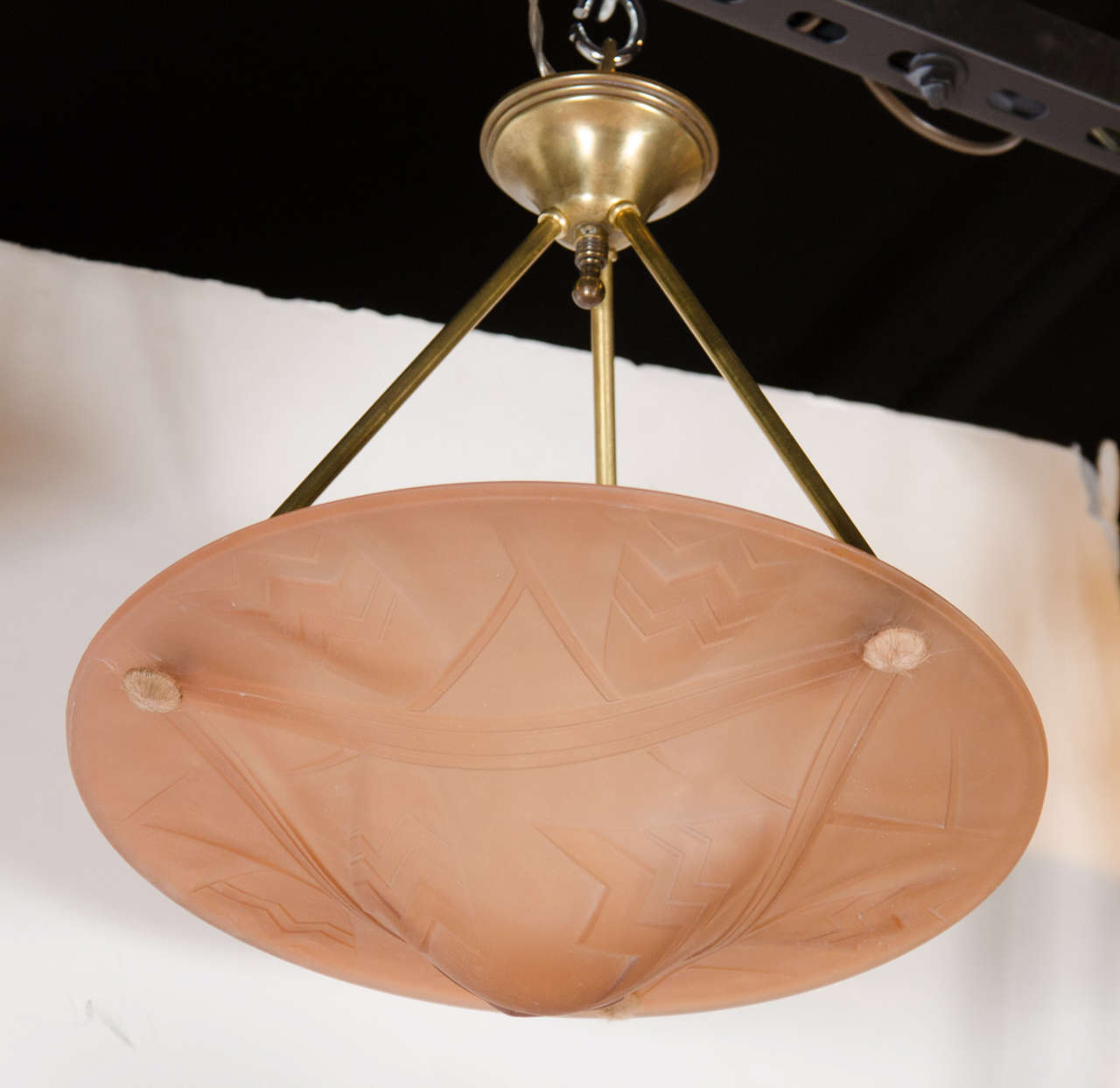 Art Deco pendant chandelier signed Degue. This exquisite pendant chandelier features a hand blown glass dome in blush copper tones with stylized geometric design that is hung from three antique brass rod supports that lead up the antique brass
