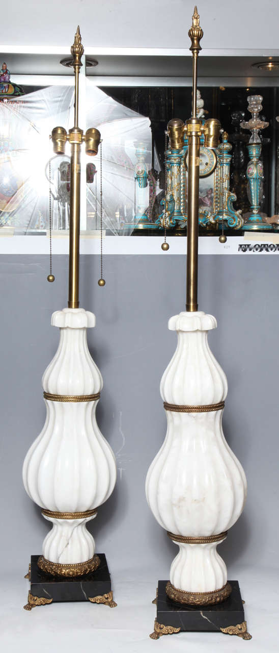 Coppia di lampade scanalate in marmo bianco e bronzo Art Deco attribuite a E. F. A Caldwell. La base in marmo nero è decorata con piedi in bronzo dorato a forma di artigli. Il bronzo è evidenziato da piccoli punti in rilievo intorno alle creste