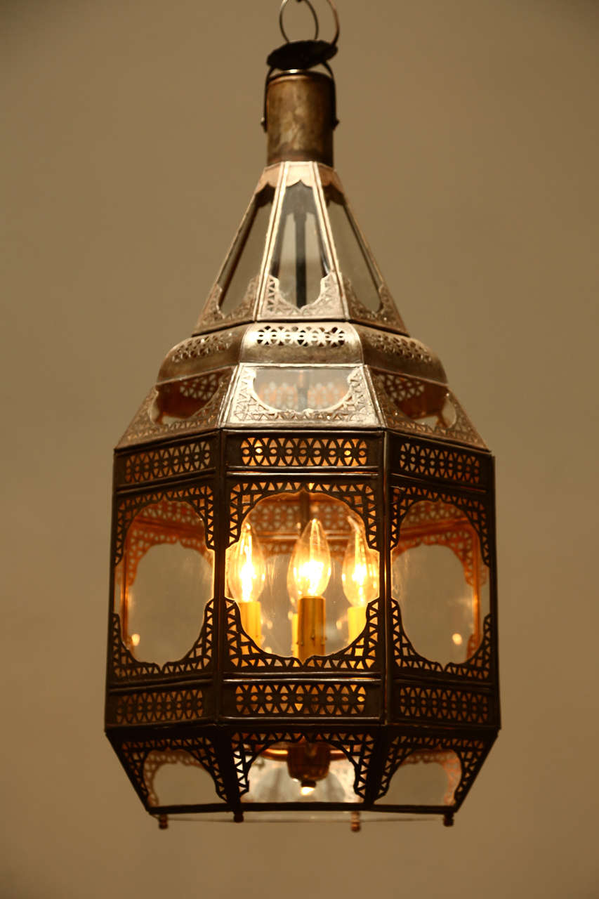 Moroccan Moorish clear glass lantern with intricate metal filigree.
Octagonal shape, delicately handcrafted by artisans in Morocco. Bronze metal color finish. Could be used hanging from the ceiling or seating on a table, or as a wall