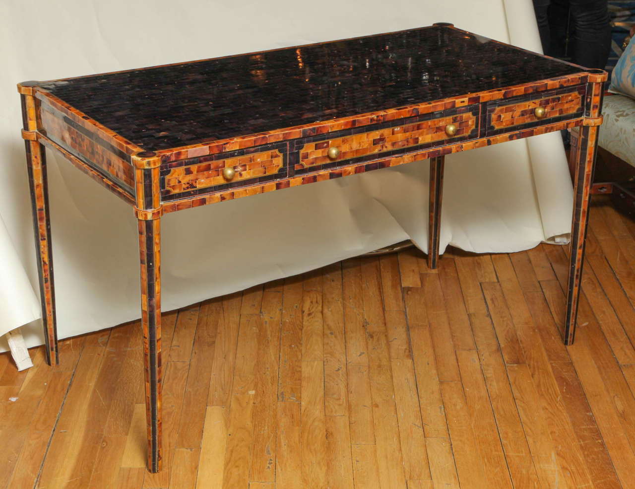 A Maitland-Smith pen shell veneered Neo-Classic design writing table with three drawers having brass pulls in apron of desk front. The drawers having patterned pen shell veneer. The top with horizontal sections of pen shell and rounded corners