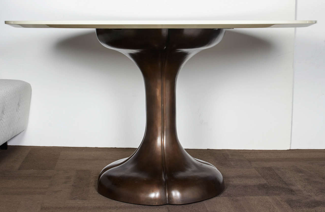 Outstanding modernist dining table with a circular top in a crème lacquered finish and with a highly stylized bronze pedestal base. The pedestal is comprised of heavy-weight cast iron with a bronze finish and features hand-forged waterlily or lotus