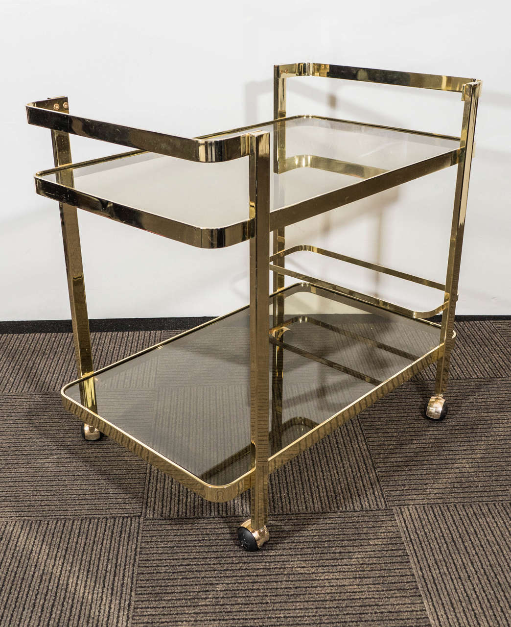A vintage two-tier bar cart, produced circa 1970's, in heavy brass stock, with smoked glass inset shelves and bottle rack, on caster wheels. Excellent vintage condition, consistent with use and age.