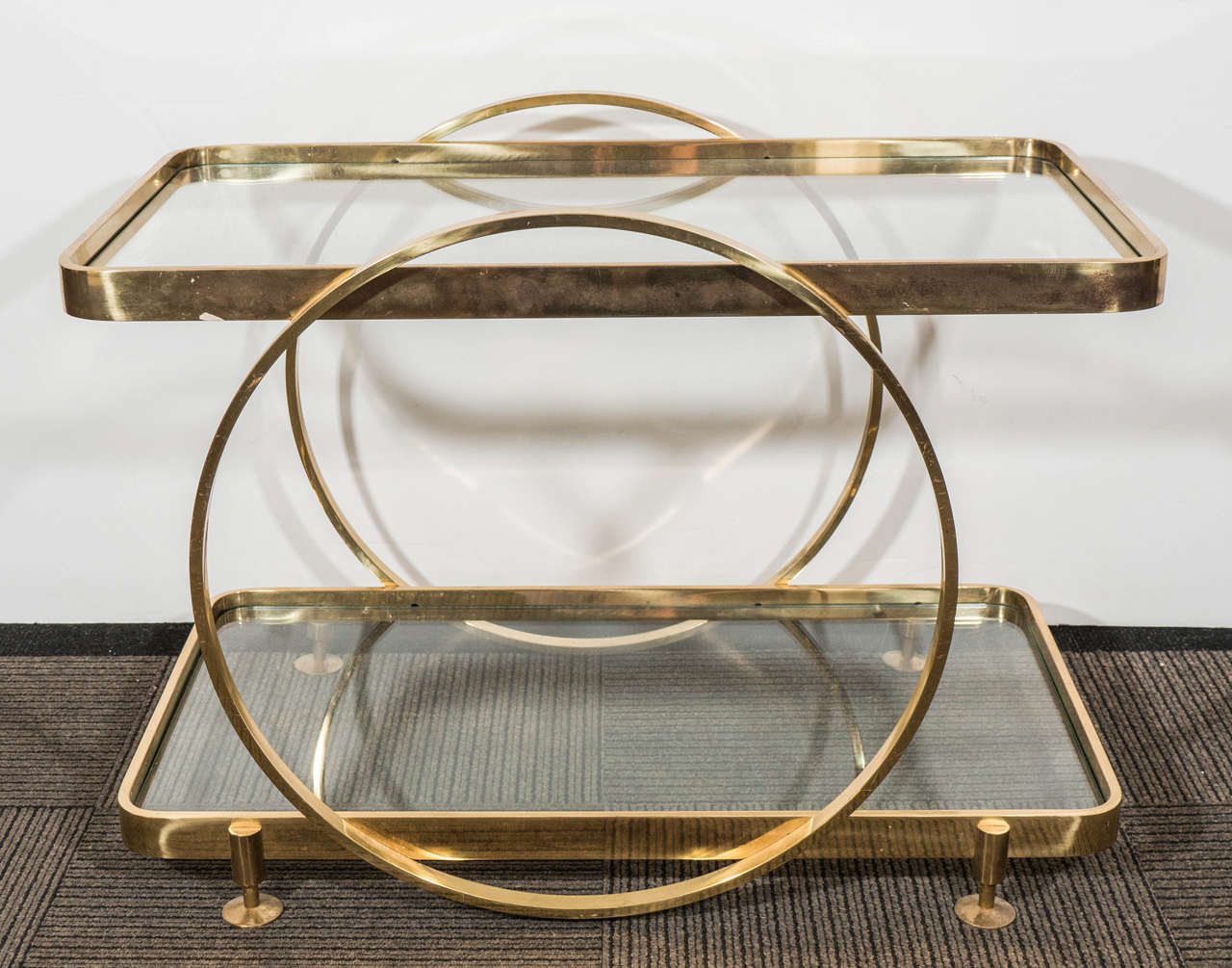 A vintage Italian two-tier serving or side table, in brass frame with glass inset shelves, supported by two flanking hoops and four circular brass feet. Good vintage condition with some age appropriate wear and minor scratches to the brass surface.