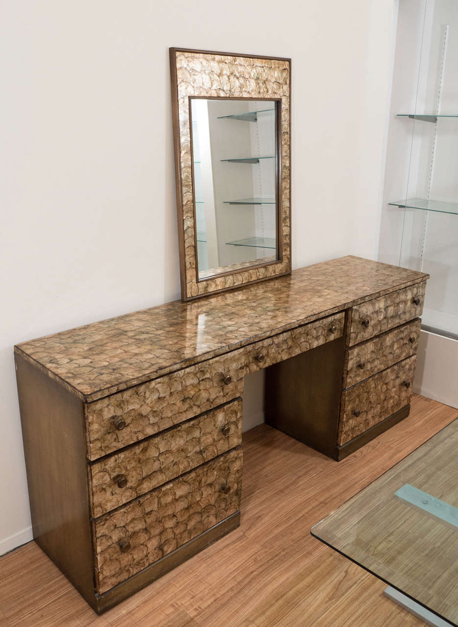 A vintage Hollywood Regency style seven-drawer vanity desk with brass knobs, with capiz shell inlay, against a painted wood frame, with matching mirror. Good vintage condition with minor scratches to surface.

Dimensions of desk: 30.5 in H x 72.75