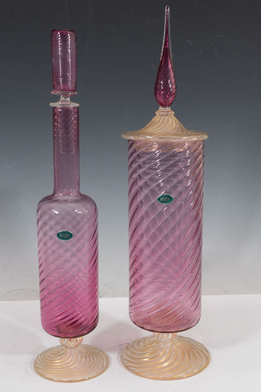 A vintage pair of decanters in Murano glass, produced by Fratelli Toso, circa 1960s, both pink and crafted in twisted form, on raised circular foot with swirling flecks of gold; one of pair has a waisted cylinder stopper and elongated neck, the