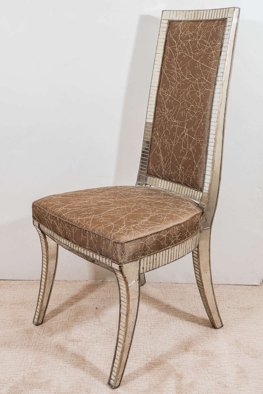 A vintage set of four dining chairs, produced circa 1950s, with mirrored panels inset against a silver painted wood frame, high rectangular backs and seats reupholstered in Calvin Klein silk, on Klismos legs. Good vintage condition, with some age