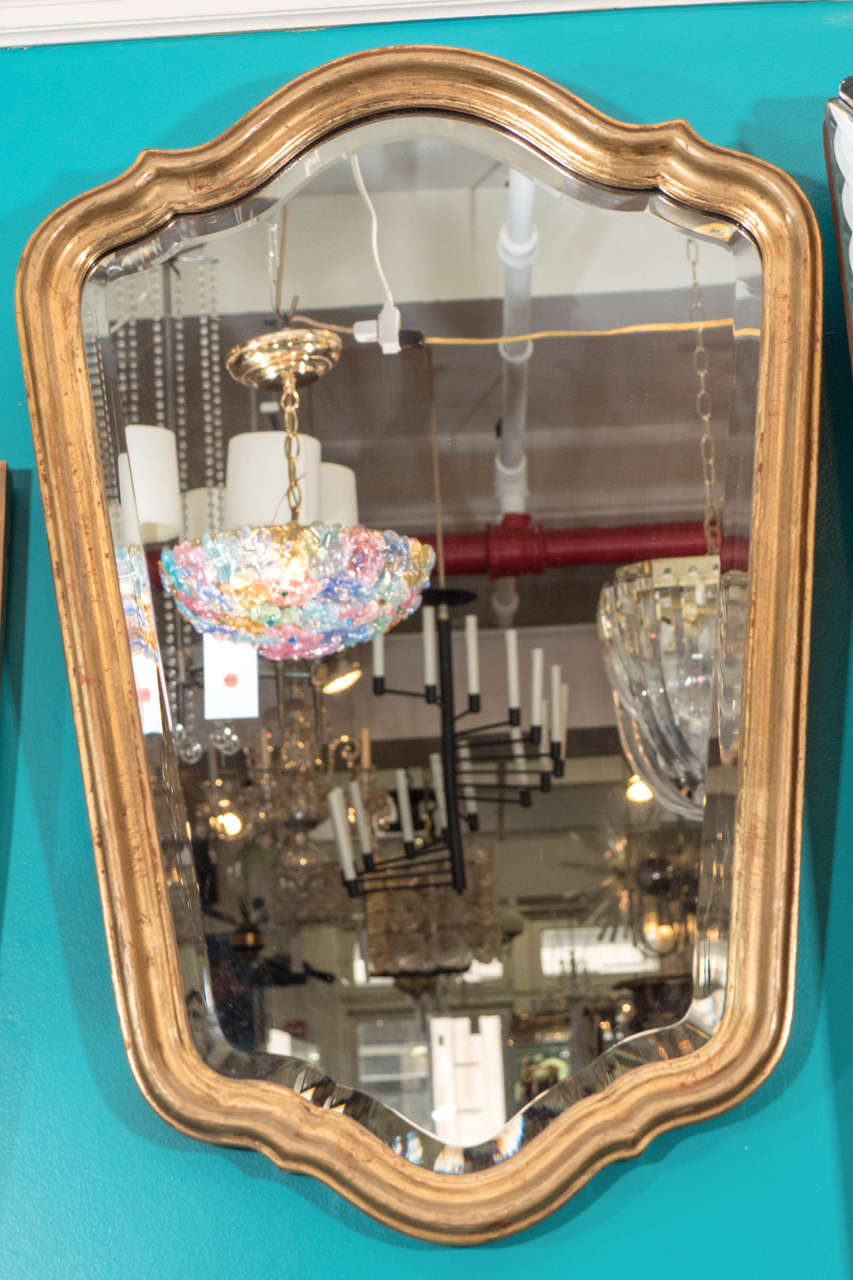 A vintage Hollywood Regency style mirror, produced circa 1940's - 1950's, with shield-form gold leaf frame designed by Kittinger Furniture Company, inset with beveled glass mirror. Good vintage condition with some age appropriate wear.