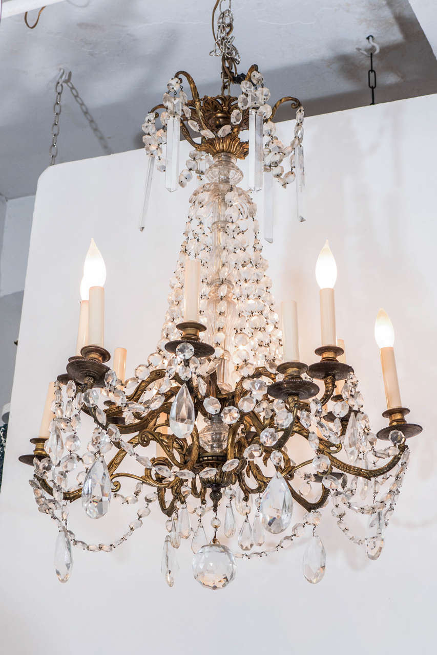 A vintage chandelier, with twelve, two-tier gilt bronze arms in scrolling acanthus leaf form, trimmed with crystal drops. Wiring and sockets to US standard, requires twelve candelabra base bulbs. Good vintage condition with some age appropriate wear