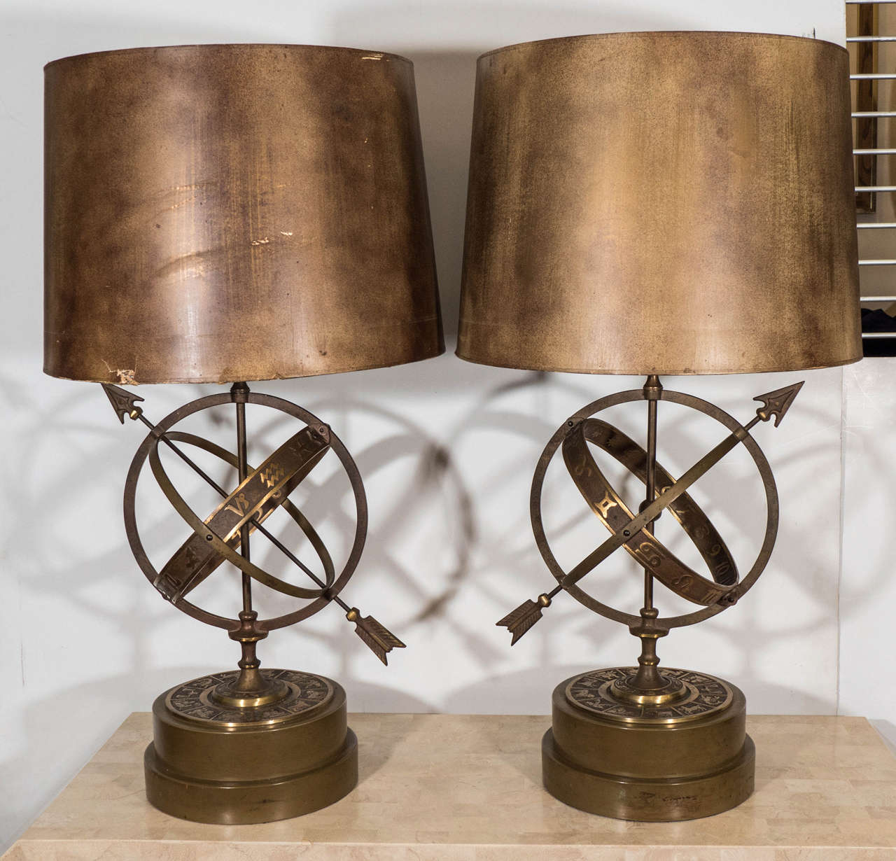 Fantastical pair of bronze table lamps in the form of celestial 'astrolabes', produced, circa 1940s, with stylistic piercing arrows, central globe and decorative signs of the zodiac, detailed against one of three surrounding crossed circular bands